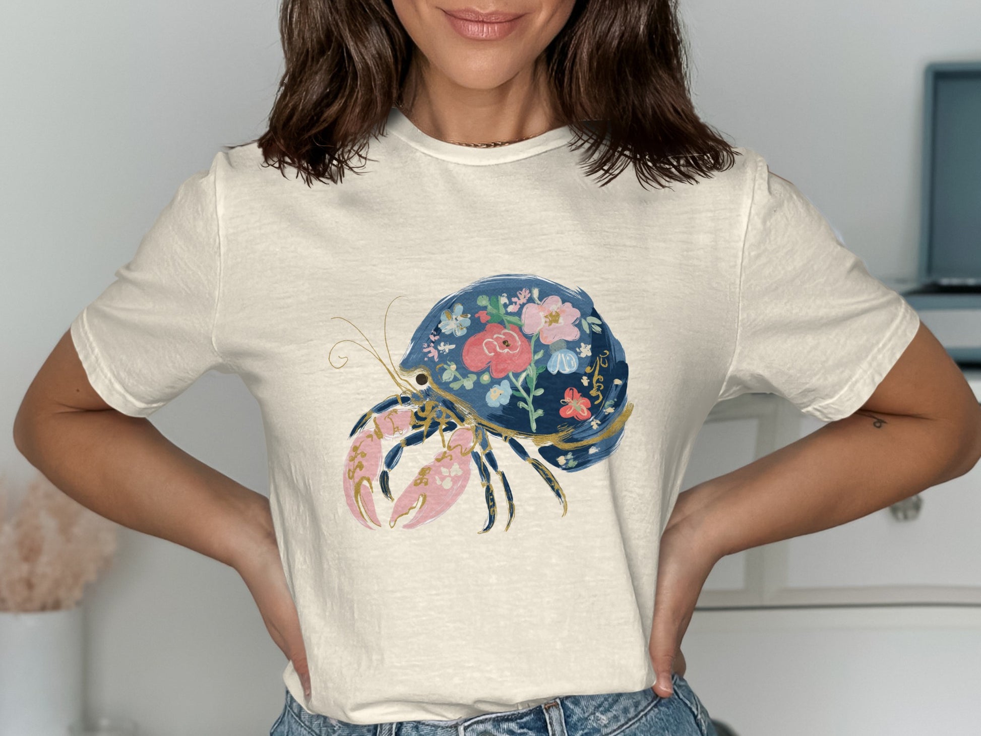 Cream t-shirt with a blue hermit crab adorned with colorful flowers.