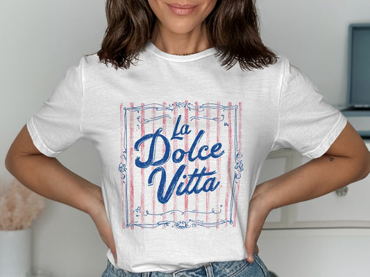 White t-shirt with "La Dolce Vita" in blue script within a red striped border.