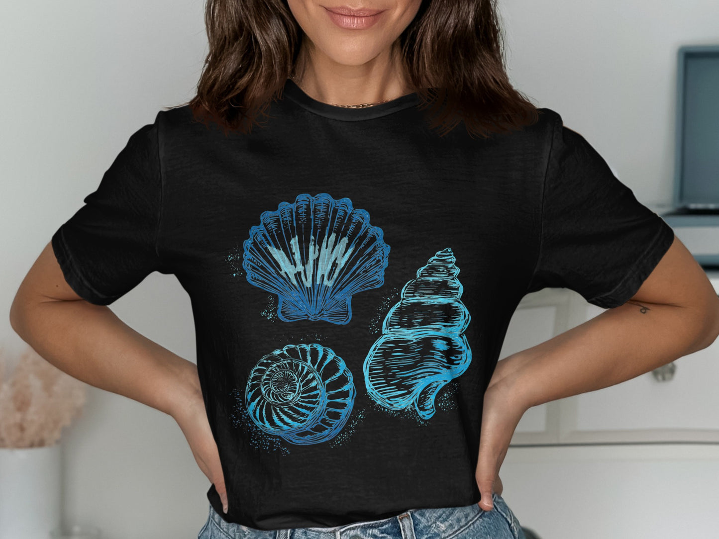 Black t-shirt with three blue watercolor-style seashells: scallop, spiral, and conch.