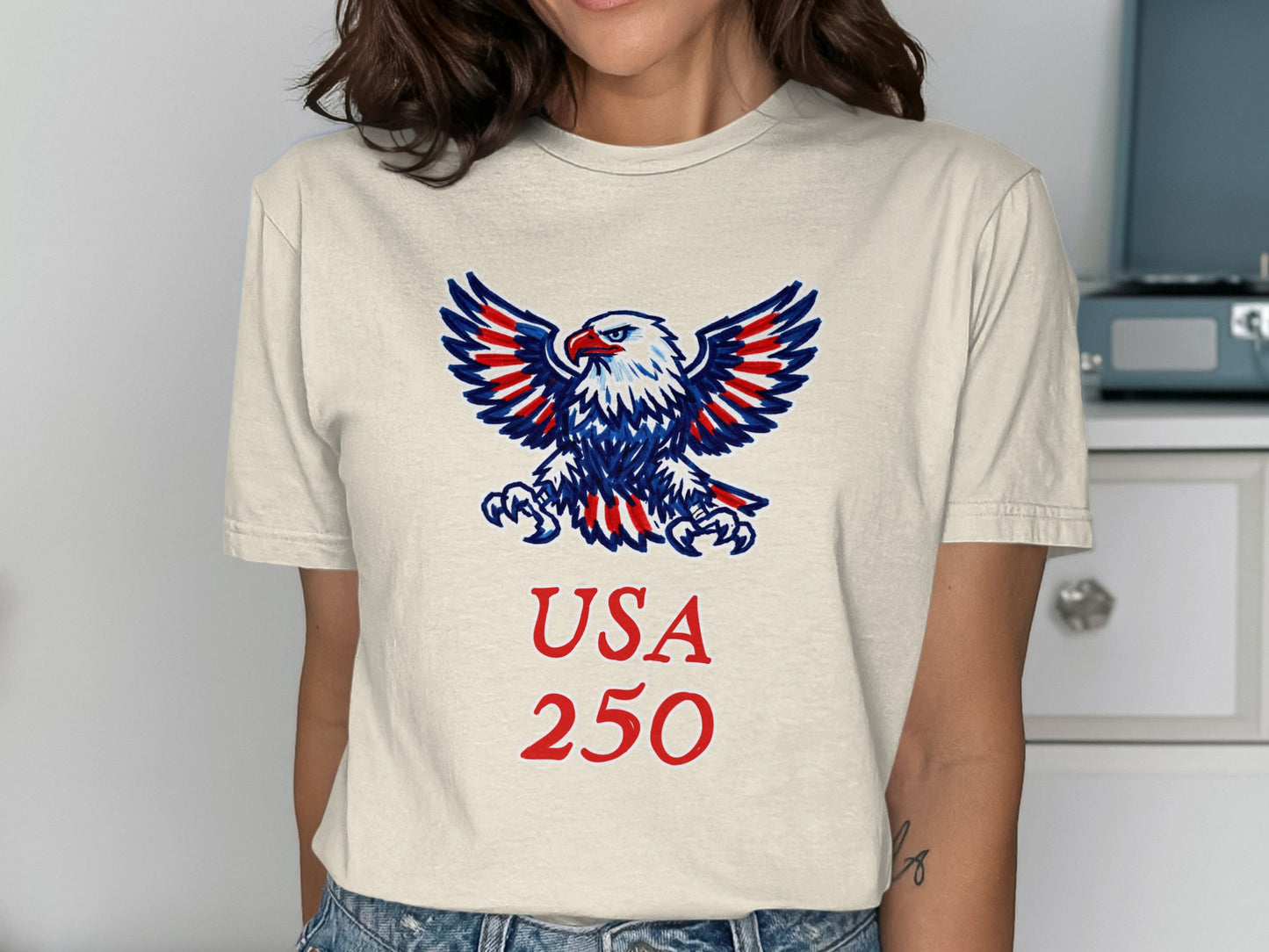 Cream t-shirt with a red, white, and blue eagle graphic and "USA 250" text.