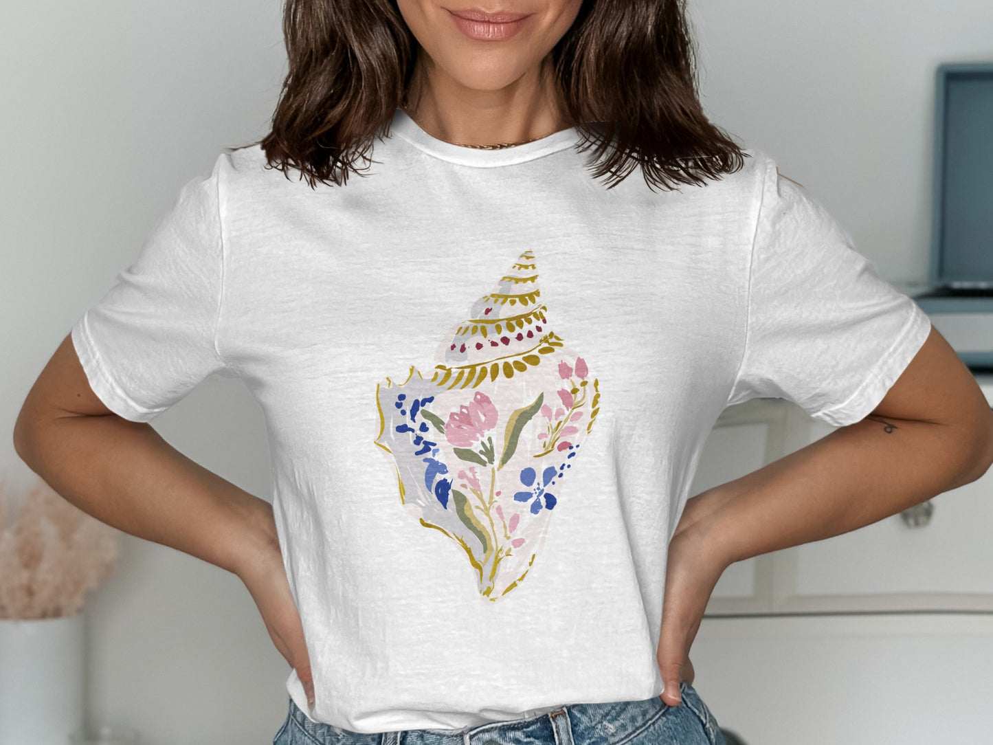 White t-shirt with a watercolor seashell illustration featuring pink and blue flowers.