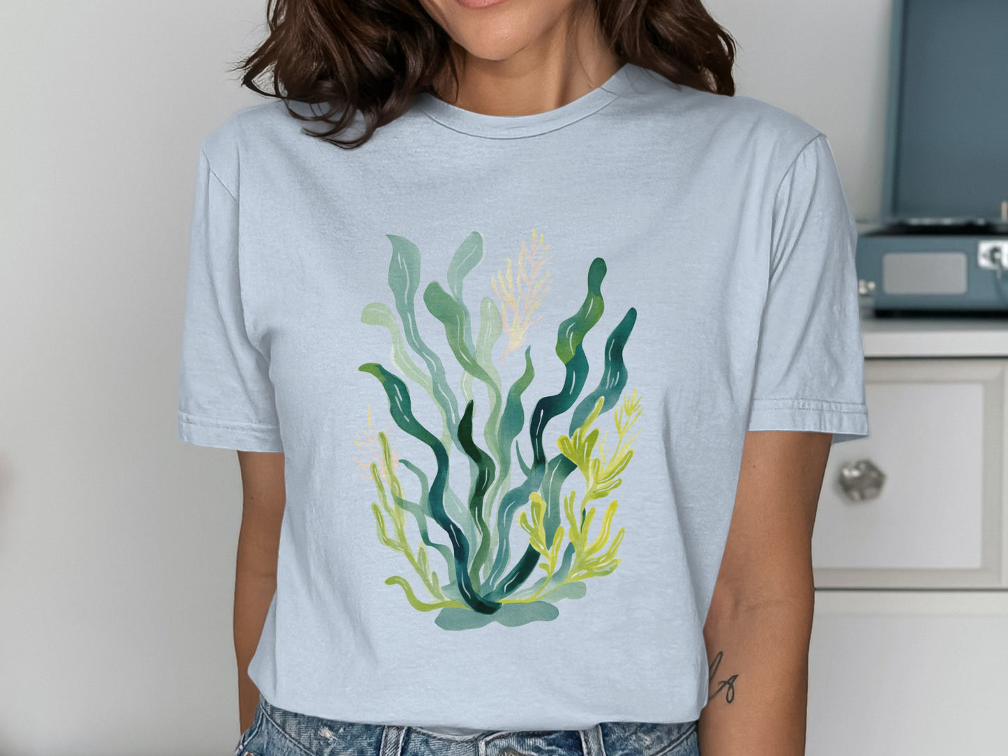 Light blue t-shirt with a watercolor illustration of green and yellow seaweed.