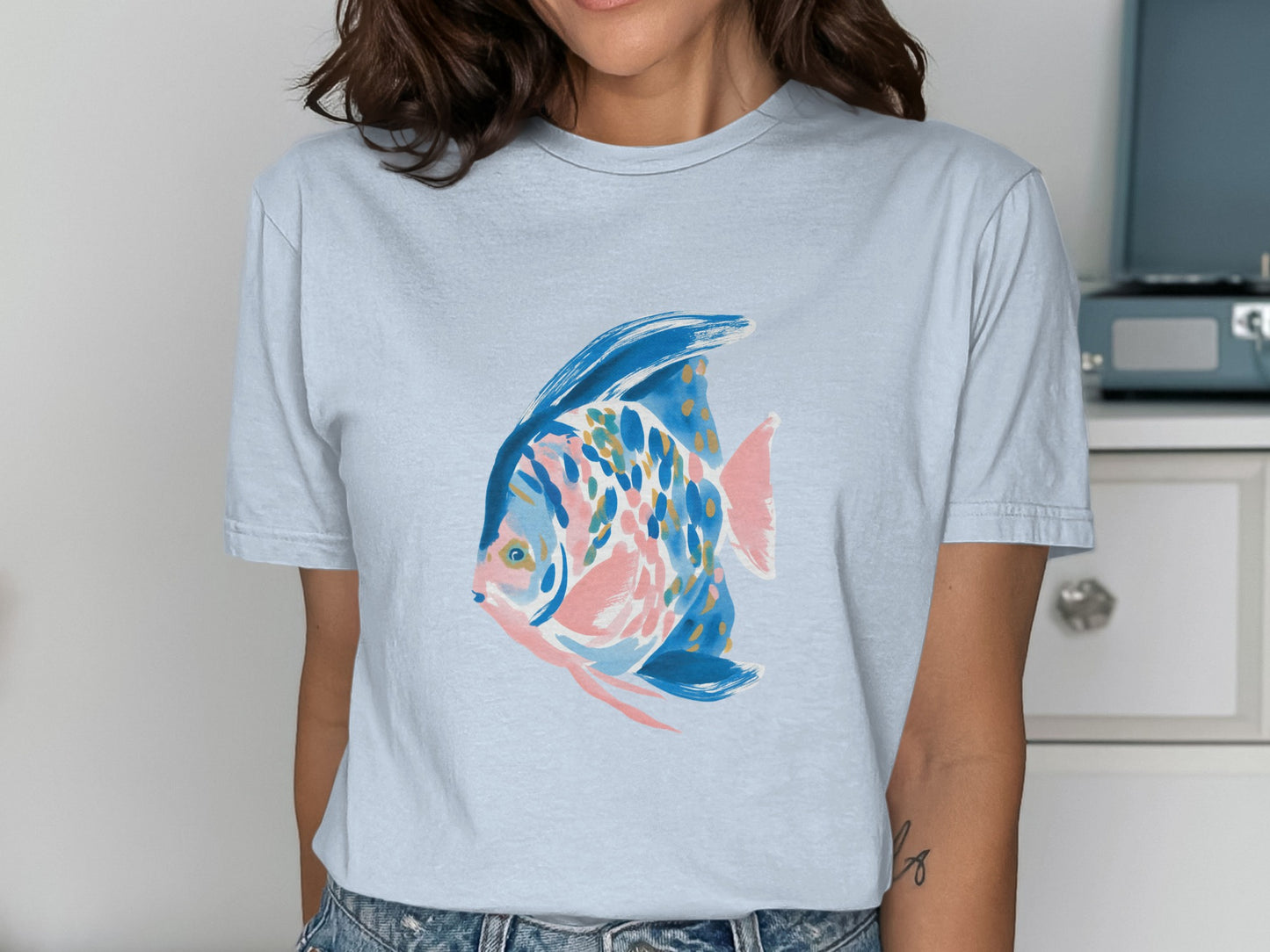 Light blue t-shirt with a watercolor-style angelfish graphic in pink, blue, and gold.