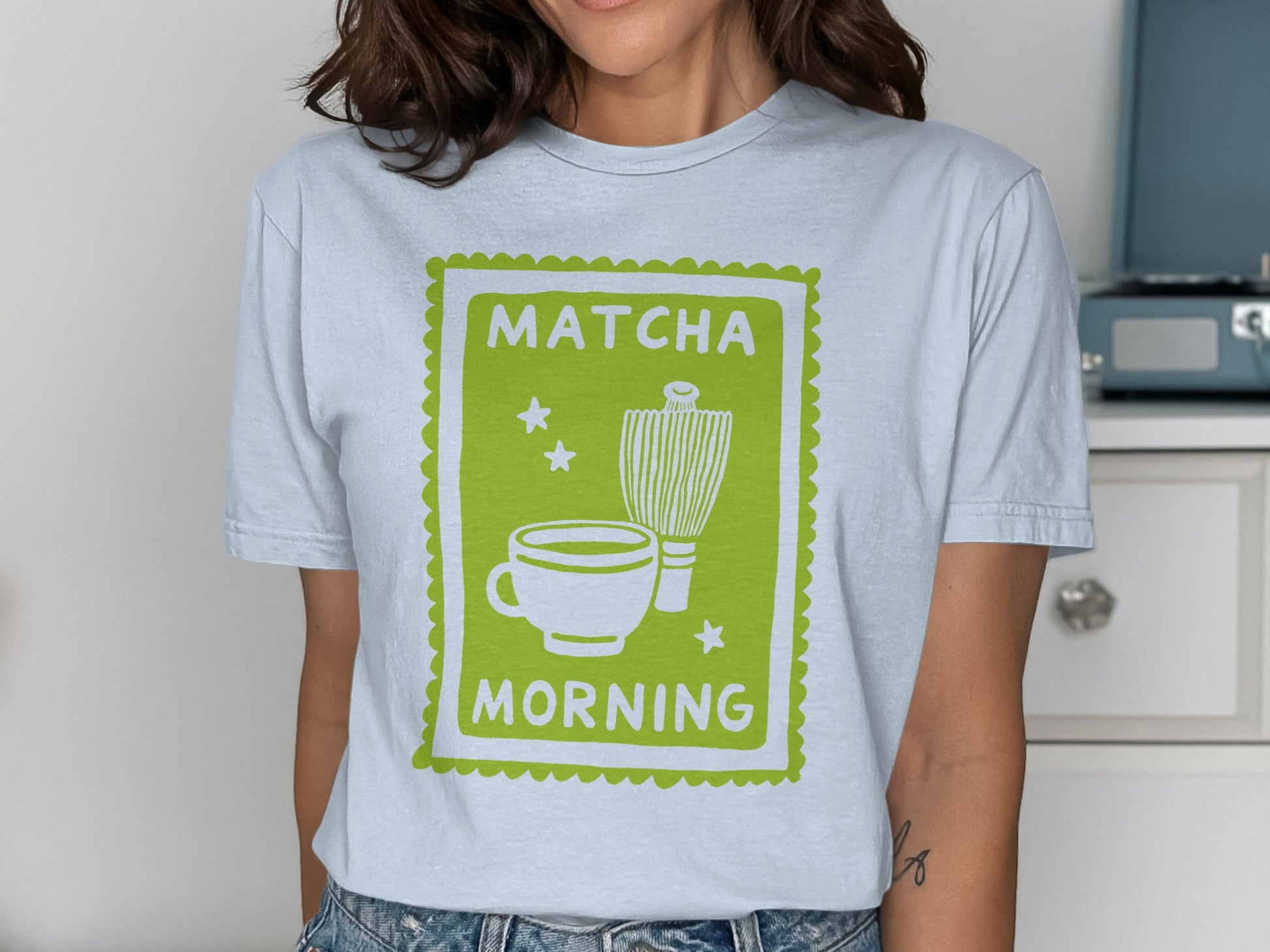 Green matcha cup, whisk, and stars graphic on white t-shirt.