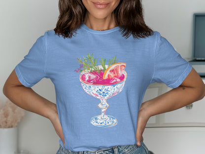 Blue t-shirt featuring a pink cocktail with garnishes in a decorative glass.