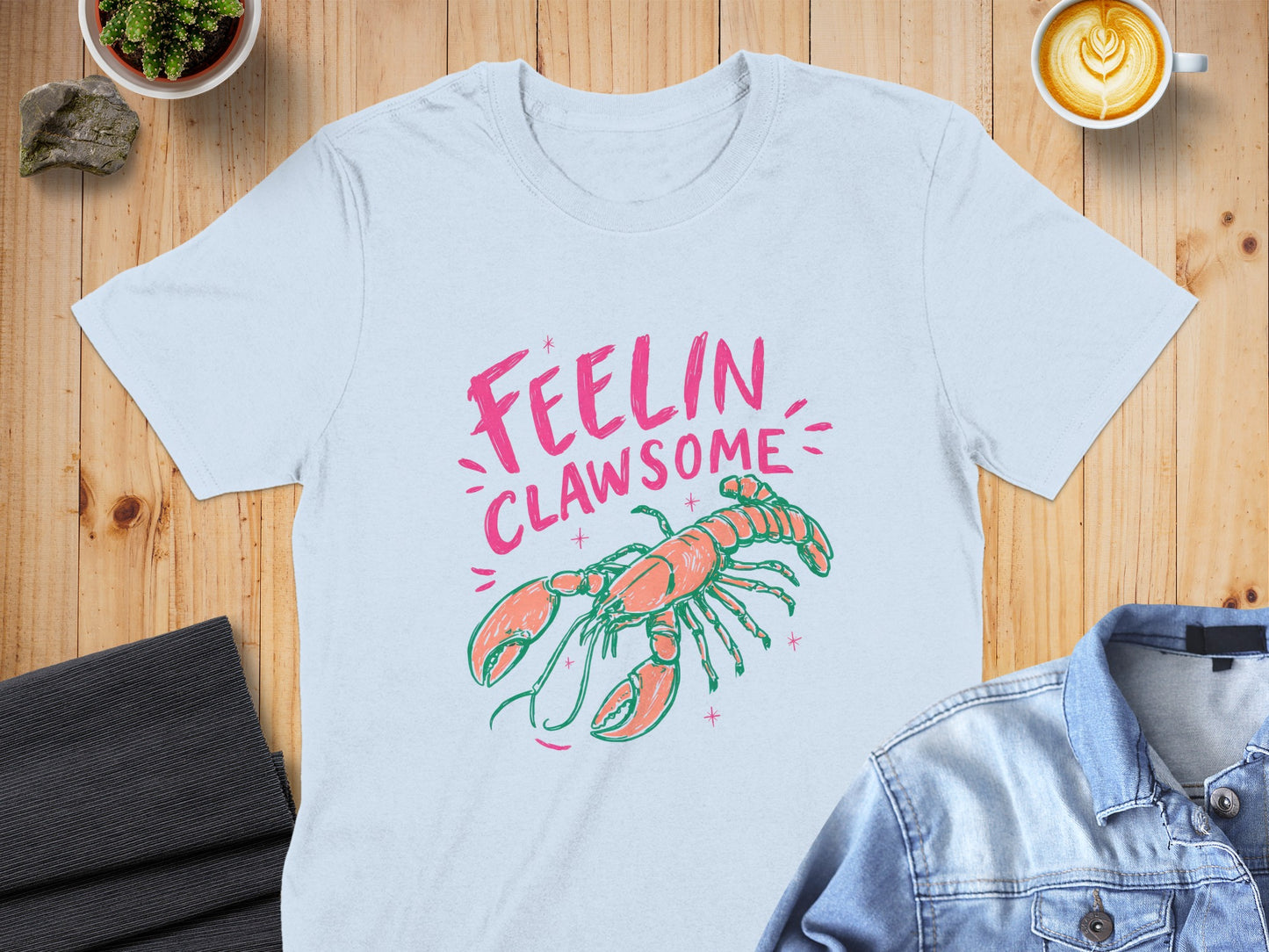 Light blue t-shirt with pink text "FEELIN CLAWSOME" and coral lobster illustration.