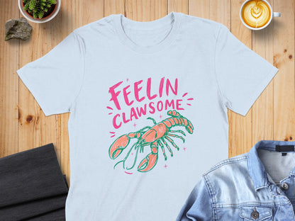 Light blue t-shirt with pink text "FEELIN CLAWSOME" and coral lobster illustration.