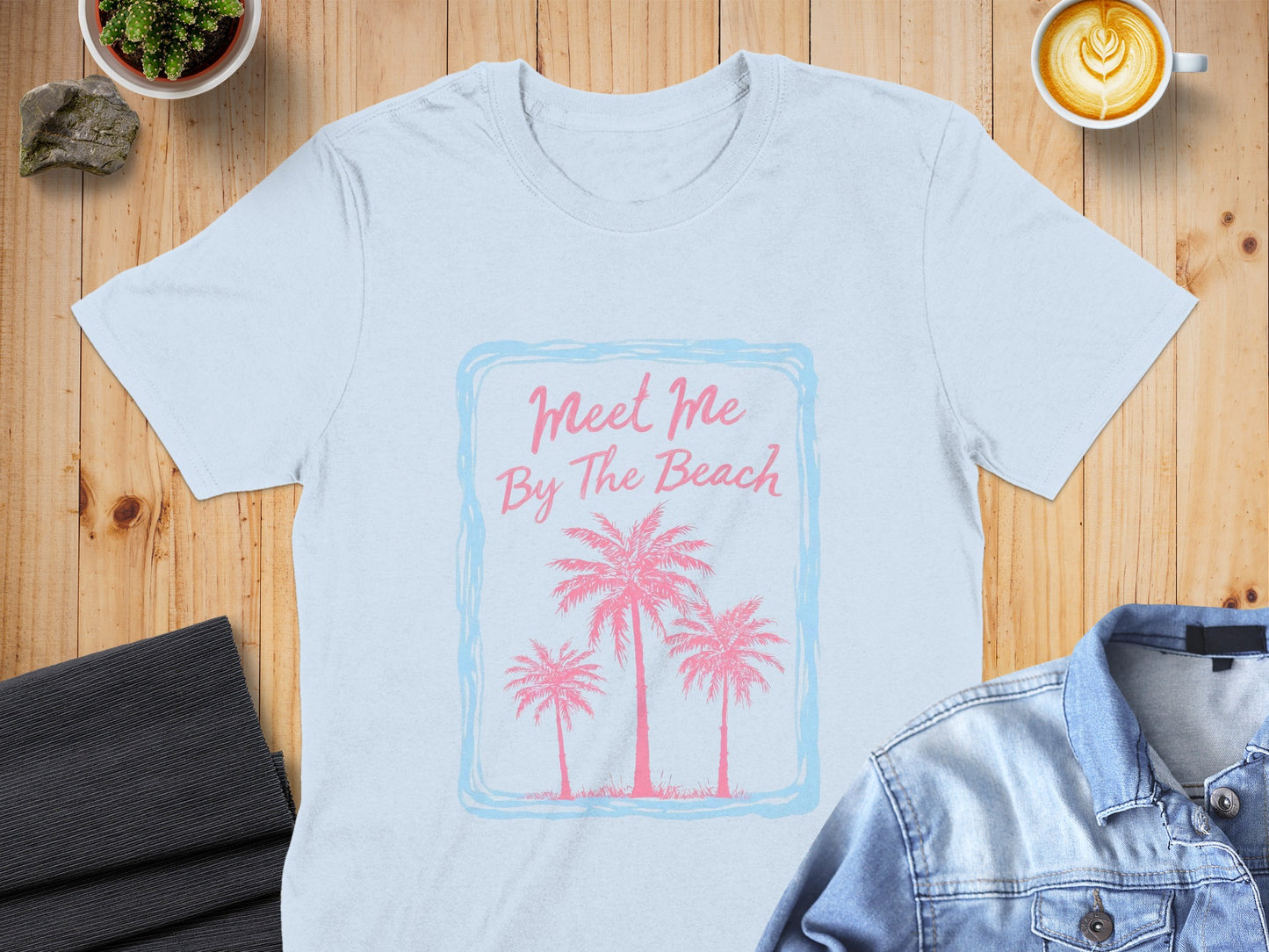 Light blue t-shirt with "Meet Me By The Beach" and palm trees graphic.