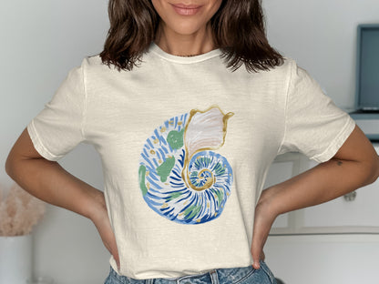 Cream t-shirt with a watercolor nautilus shell graphic in blue and green.