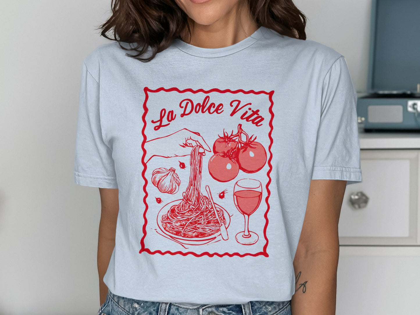 T-shirt featuring a graphic of pasta, tomatoes, garlic, and wine with "La Dolce Vita" text.