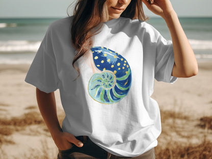 White t-shirt with a painted blue and green seashell with yellow dots.