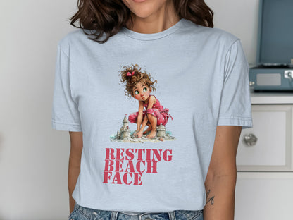 Girl in pink plays with sand on a light blue t-shirt with text.