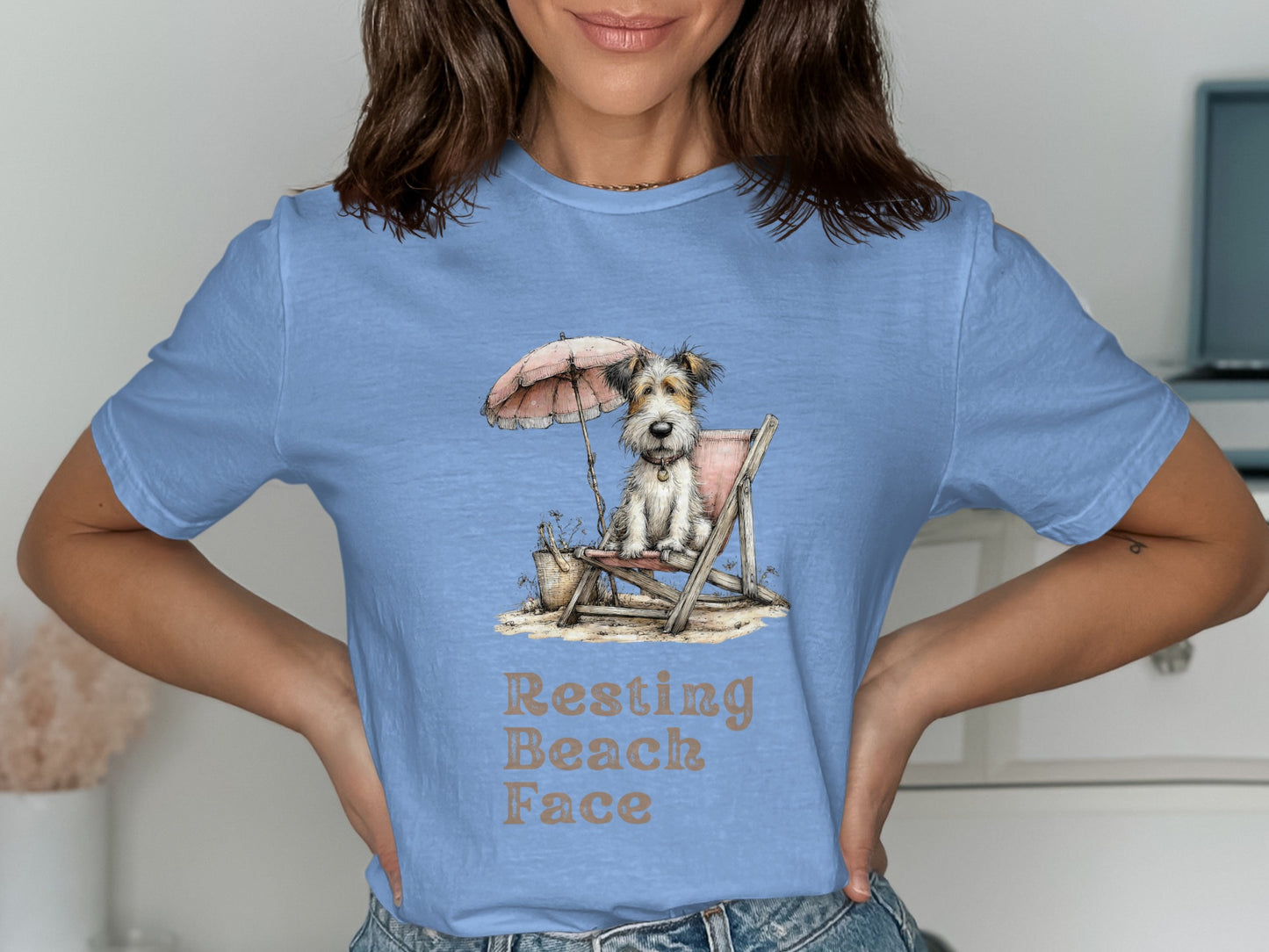 Light blue t-shirt with a dog sitting on a beach chair under an umbrella.