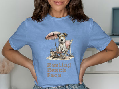 Light blue t-shirt with a dog sitting on a beach chair under an umbrella.