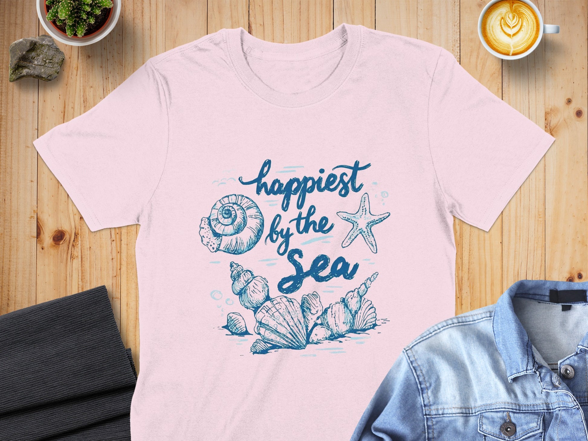 Pink t-shirt with blue watercolor "happiest by the sea" text and shell illustration.