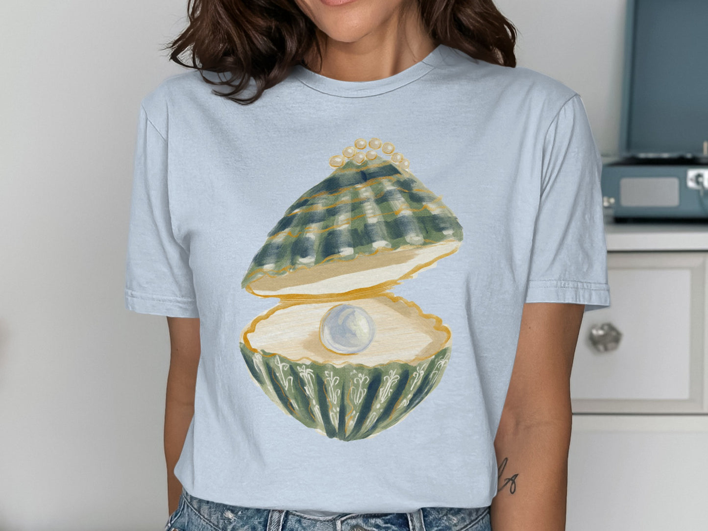 Light blue t-shirt with a watercolor illustration of an open oyster revealing a pearl.