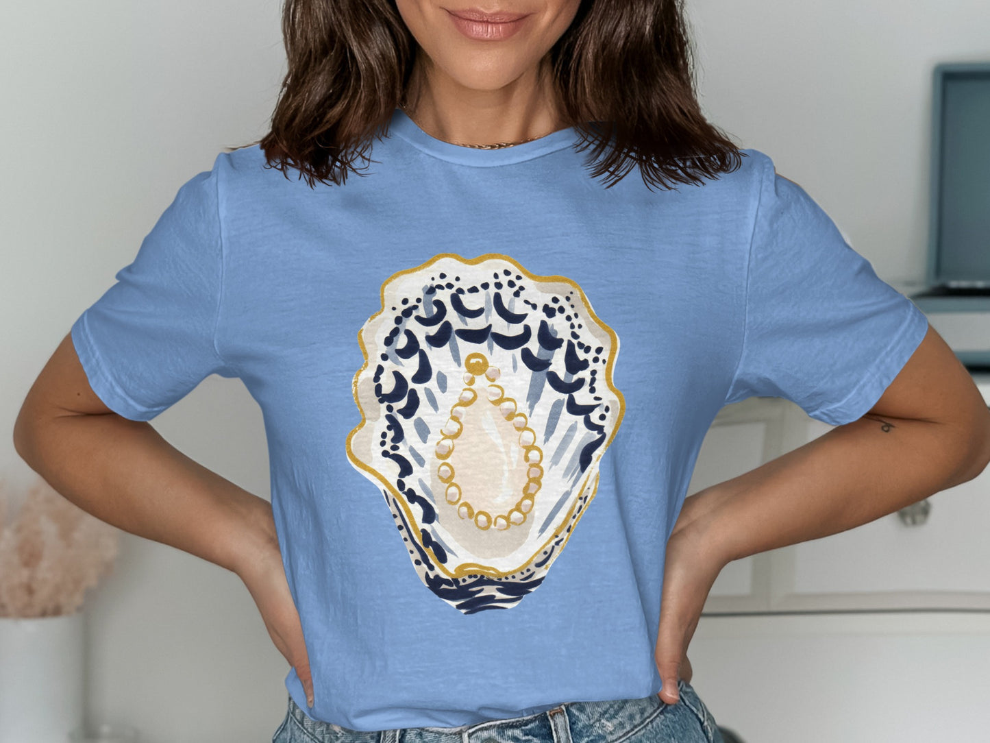 Light blue t-shirt featuring a large, stylized oyster shell with pearls and blue accents.