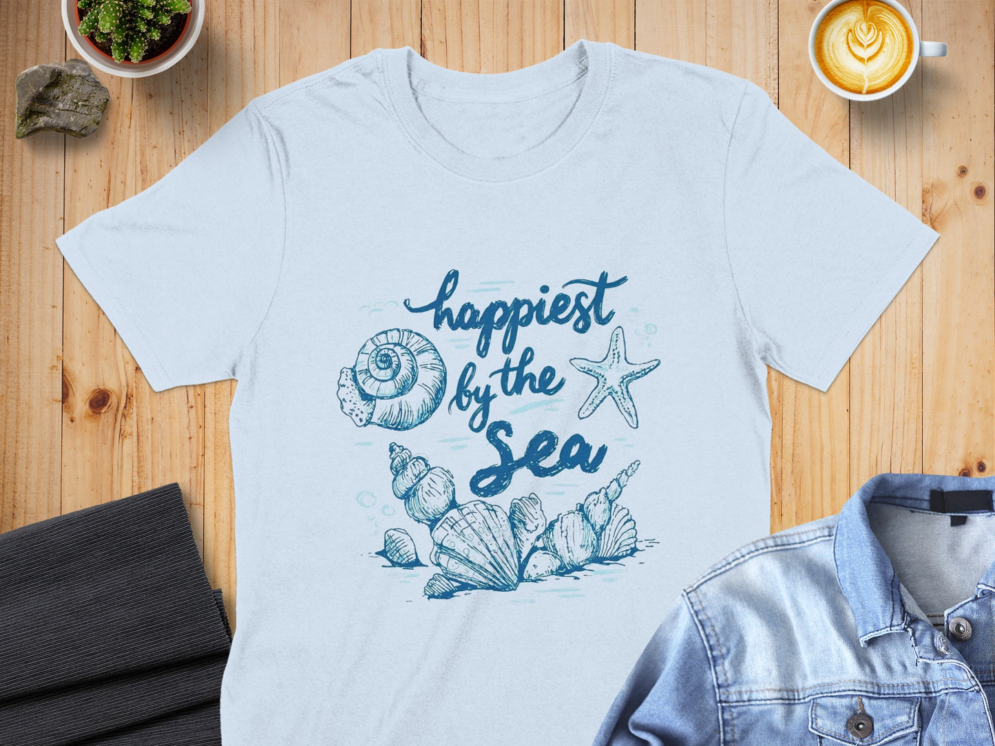 Light blue t-shirt with "happiest by the sea" and seashell graphic.