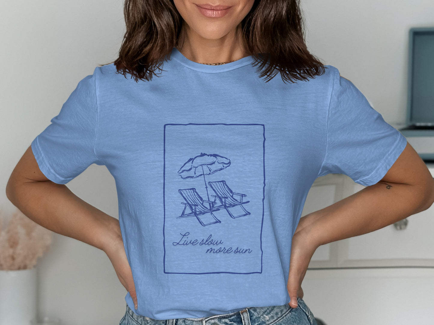Blue t-shirt with sketch of beach chairs and umbrella, text "Live slow more sun".