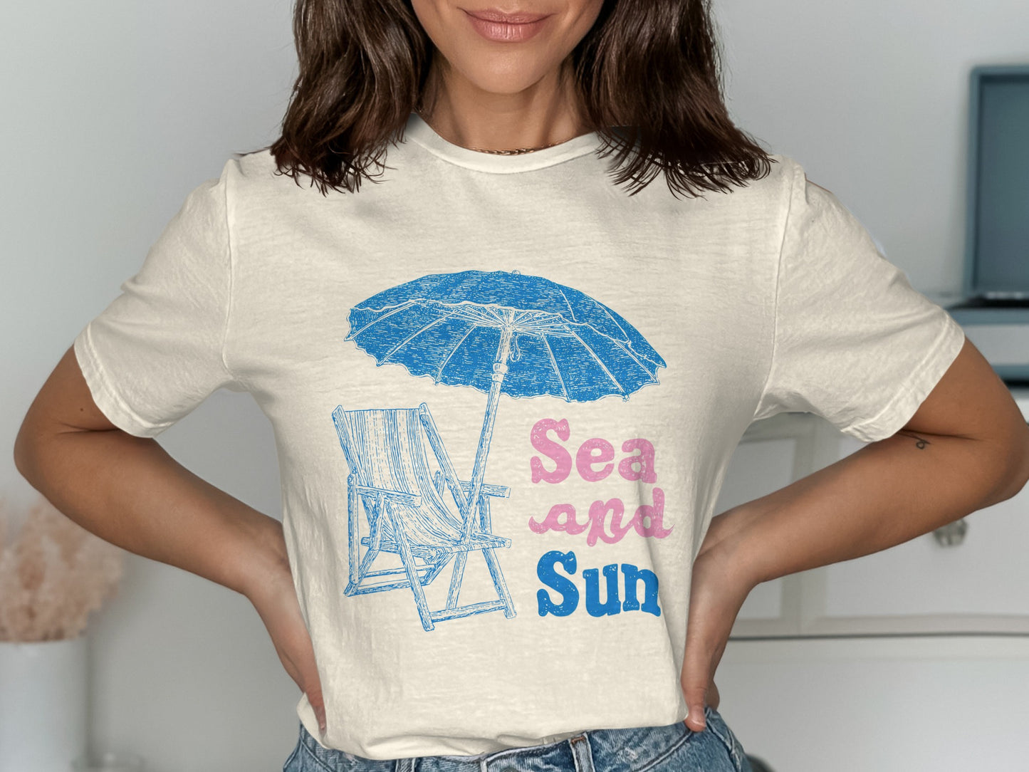 Cream t-shirt with a blue beach umbrella, chair, and "Sea and Sun" text.