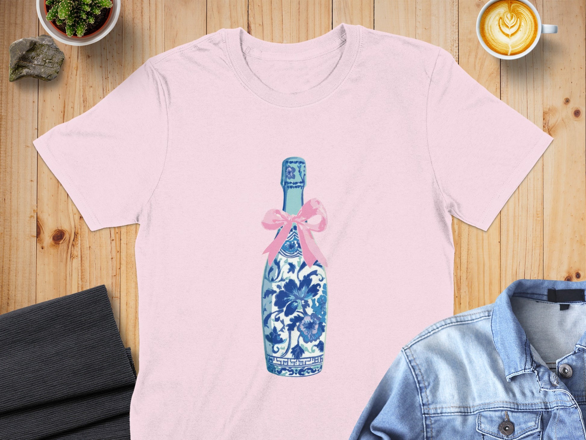 Pink t-shirt featuring a blue and white floral patterned champagne bottle with a pink bow.