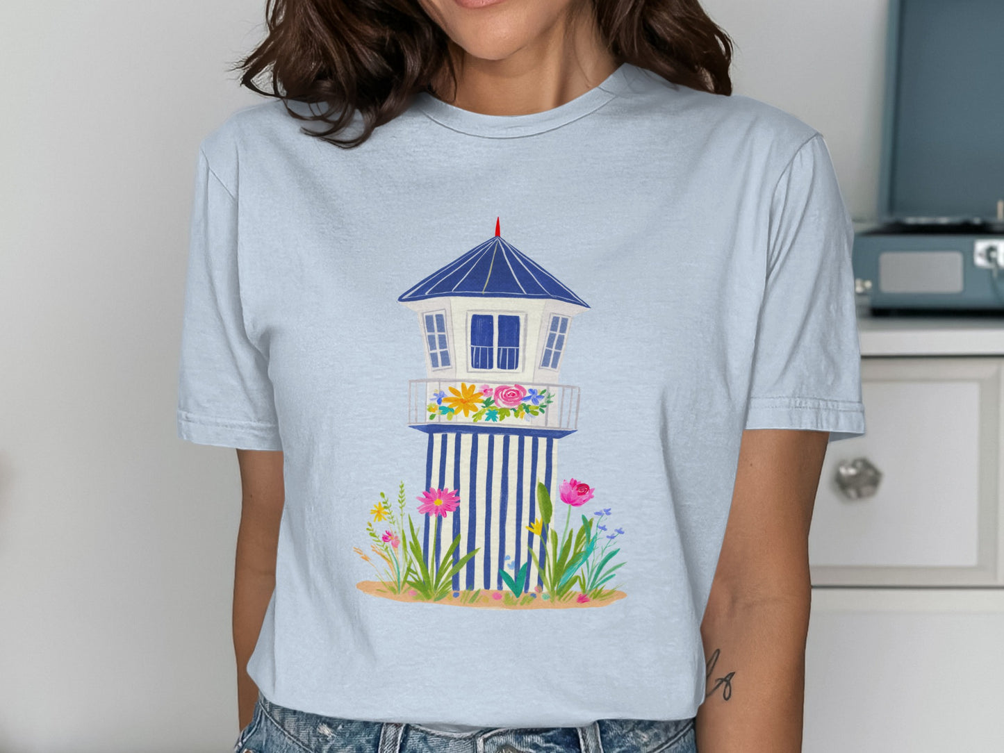 Light blue t-shirt with a graphic of a white lifeguard stand with blue stripes and flowers.