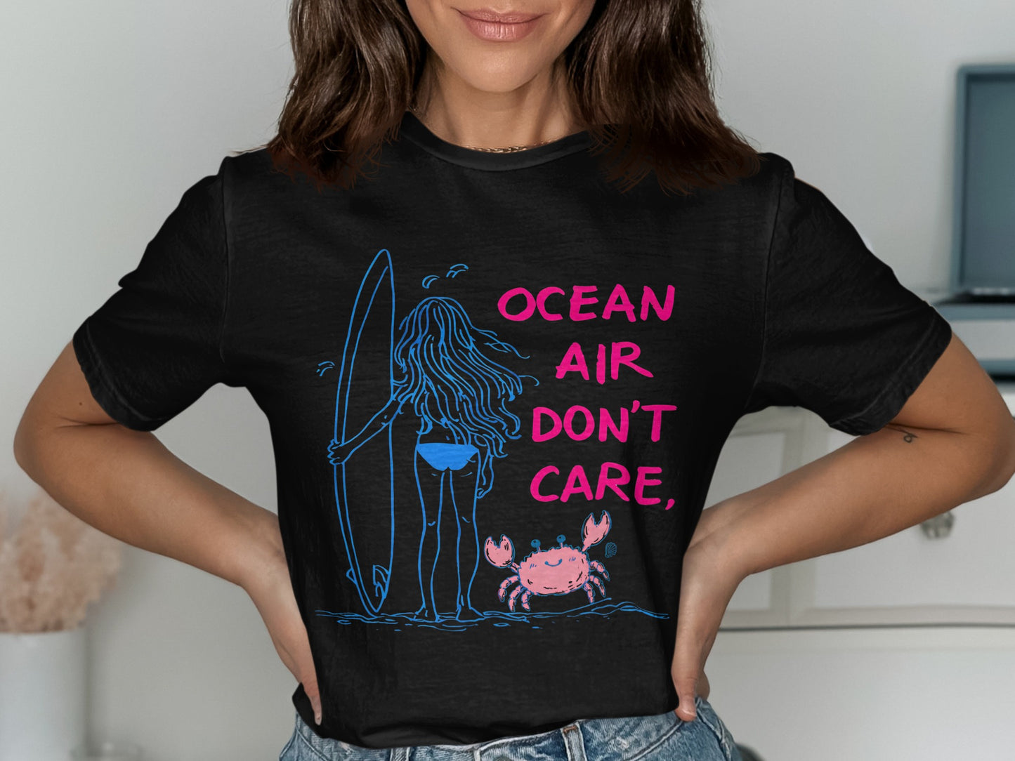 Black t-shirt with graphic of a surfer, surfboard, and crab with "Ocean Air Don't Care" text.