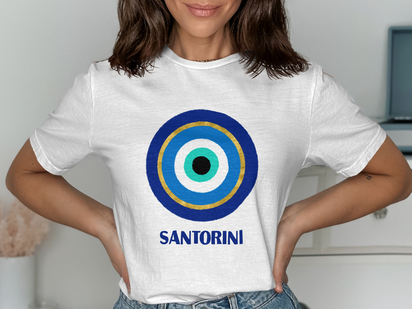 White t-shirt with blue and gold evil eye design and "SANTORINI" text.
