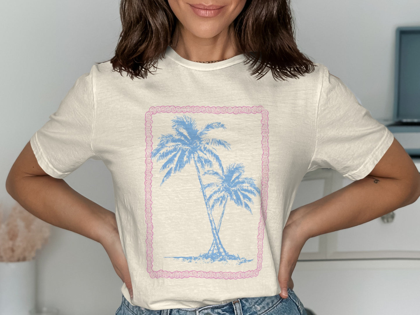 Cream t-shirt with two blue palm trees inside a pink border.