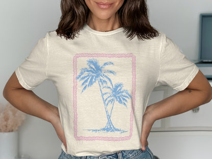 Cream t-shirt with two blue palm trees inside a pink border.
