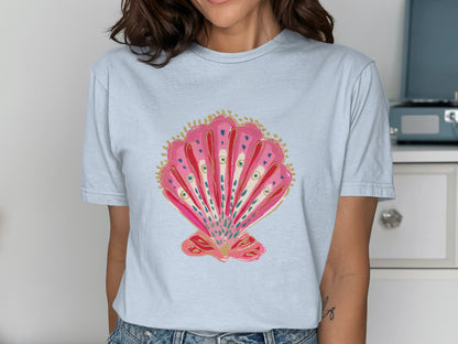 Pink seashell graphic with blue and gold accents on a light blue t-shirt.