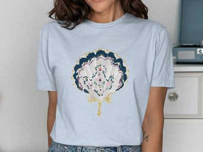 Light blue t-shirt with a decorative seashell graphic in blue, pink, and gold.