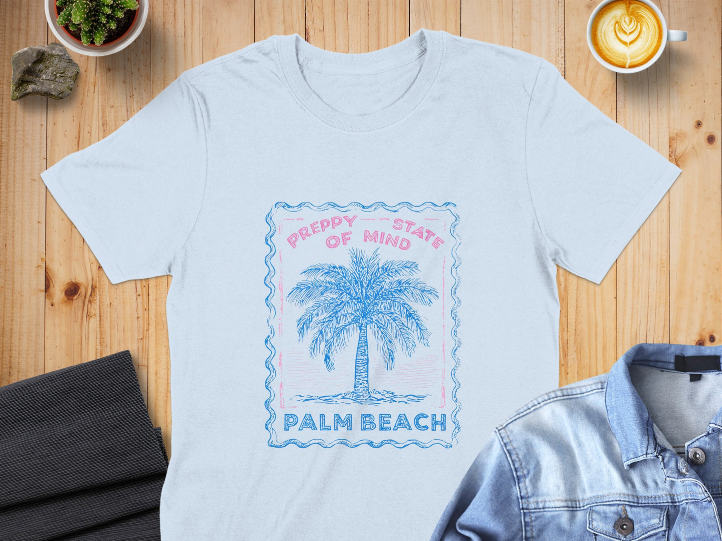 Light blue t-shirt with a pink and blue palm tree graphic and text.