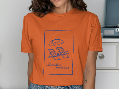 Orange t-shirt with a blue line drawing of beach chairs and umbrella, with text "Live slow, more sun."