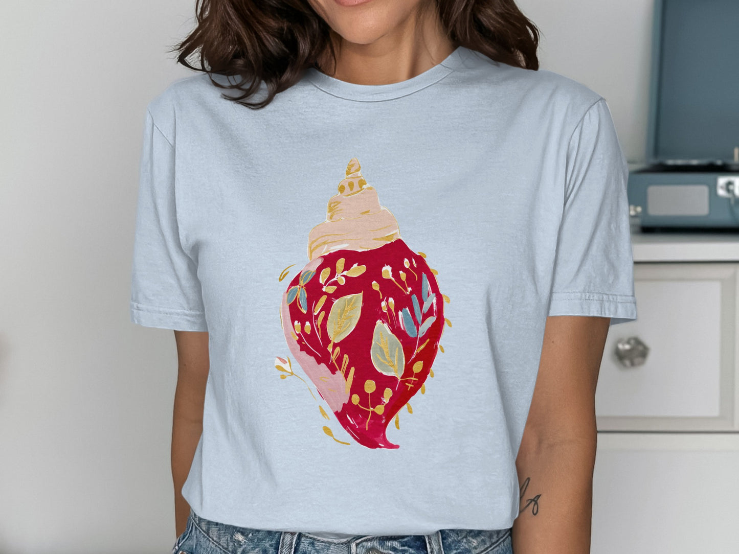 Light blue t-shirt with a painted seashell design featuring floral accents.