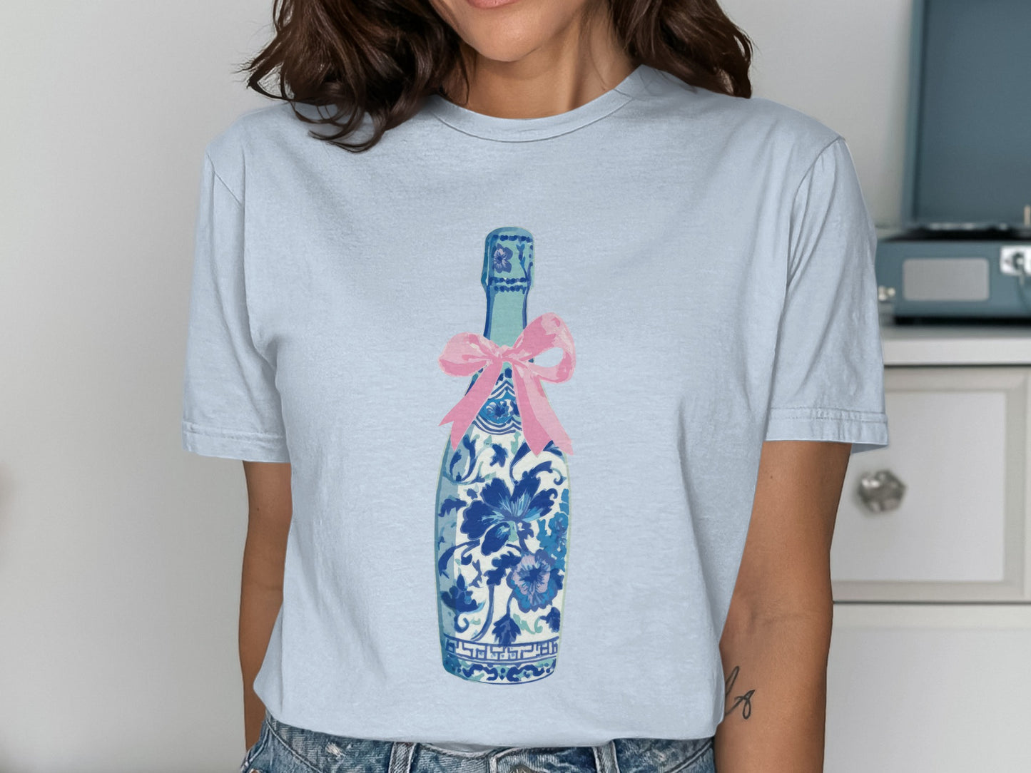 Light blue t-shirt with a blue and white floral patterned bottle and pink bow.