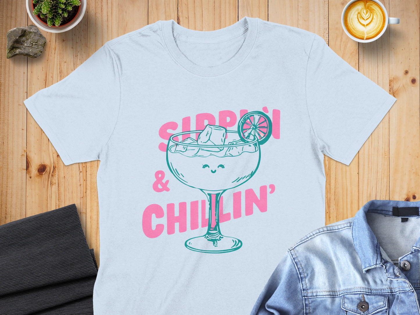 Light blue t-shirt with pink text and graphic of a smiling cocktail glass.