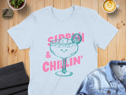 Light blue t-shirt with pink text and graphic of a smiling cocktail glass.