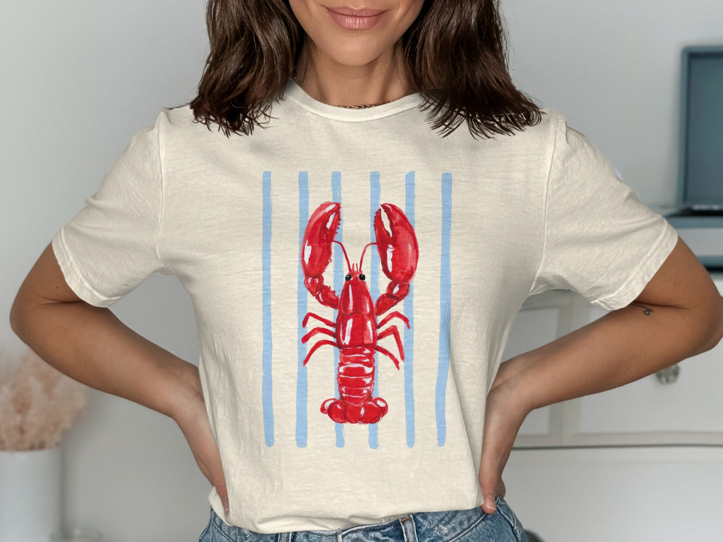 Cream t-shirt with red lobster graphic on blue stripes.