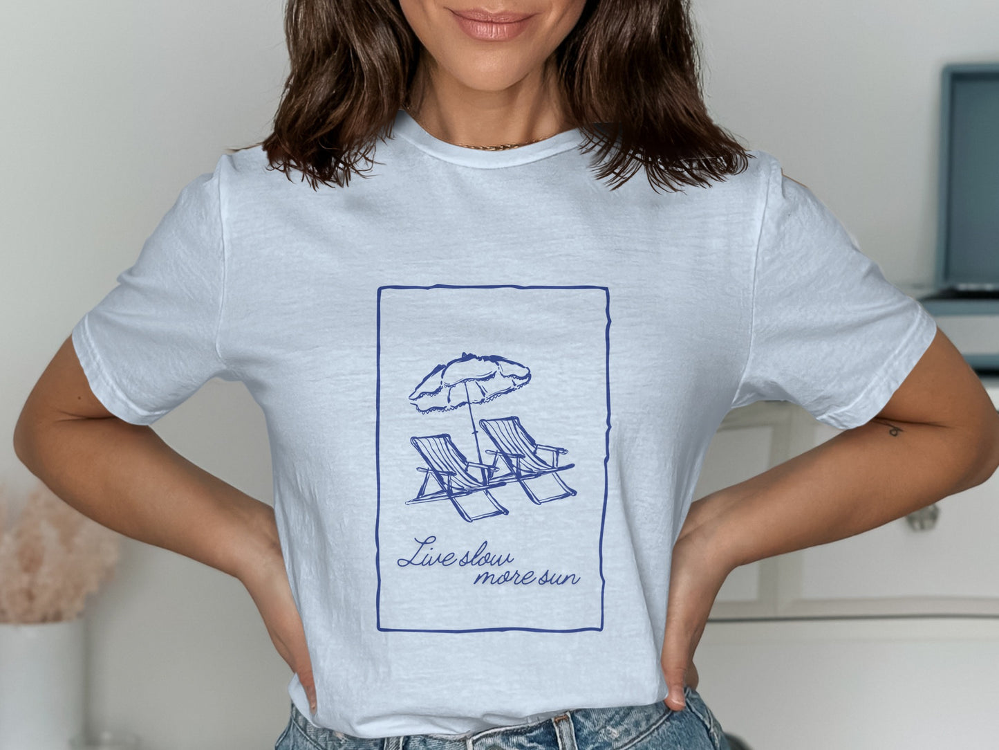 White t-shirt with blue graphic of beach chairs and "Live slow, more sun" text.