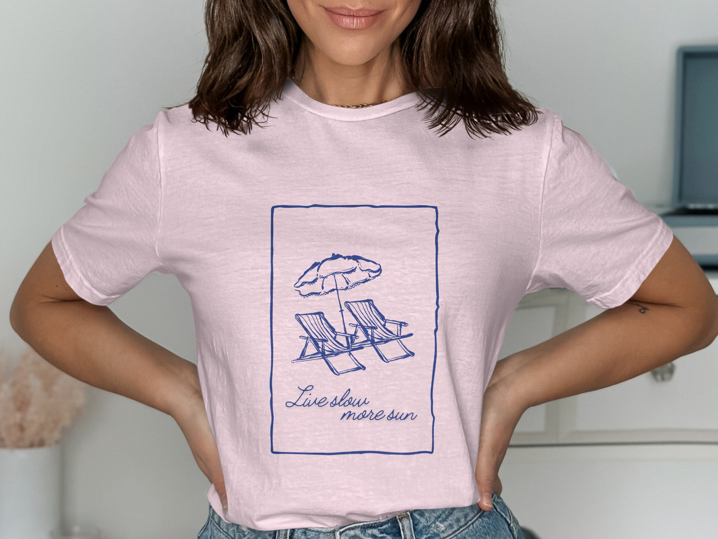 Light pink t-shirt with a navy blue outline of two beach chairs and a sun, with text.