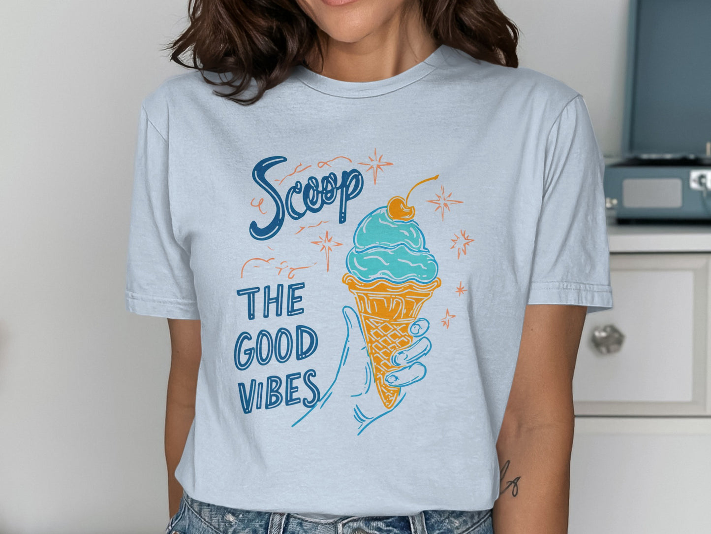 Woman wearing a light blue t-shirt with "Scoop The Good Vibes" and an ice cream cone.