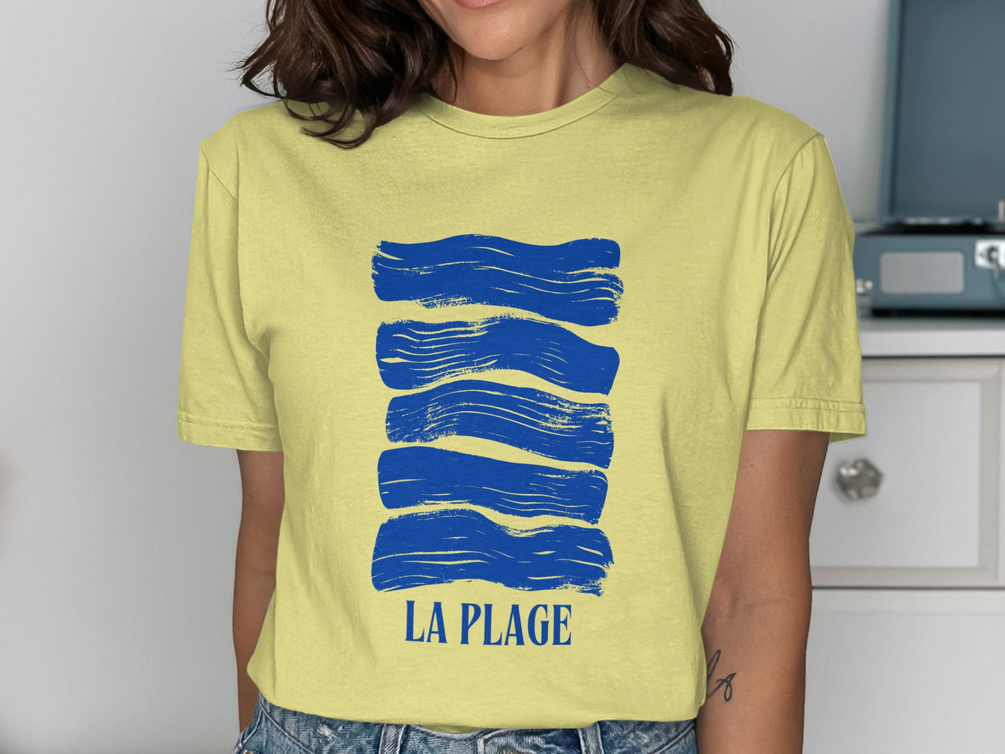 Yellow t-shirt with blue brushstroke waves and "LA PLAGE" text.