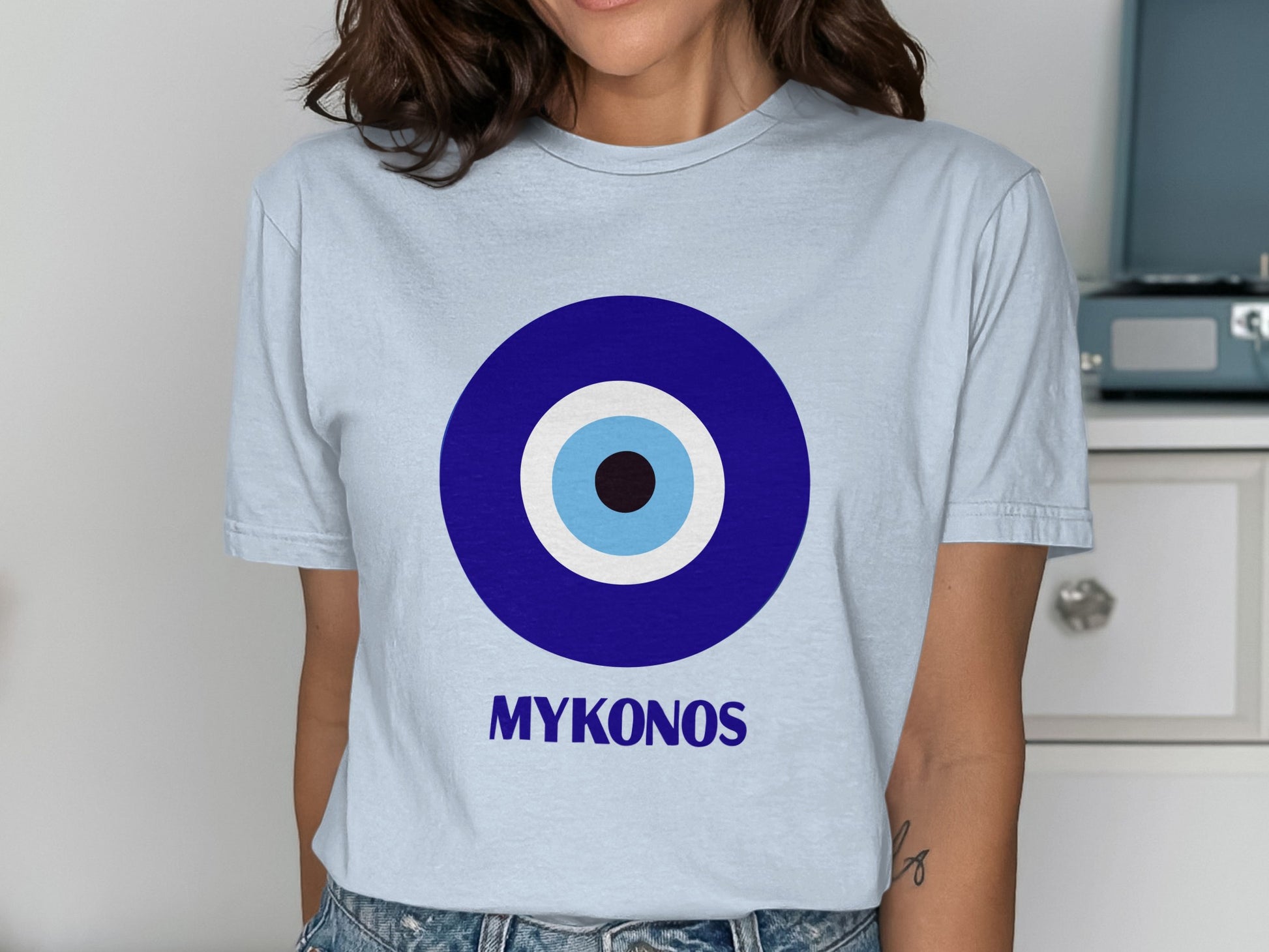 Light blue t-shirt with a large blue and white evil eye symbol and "MYKONOS" text.
