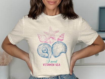 Cream t-shirt with blue and pink seashells and starfish graphic, "I need Vitamin Sea".