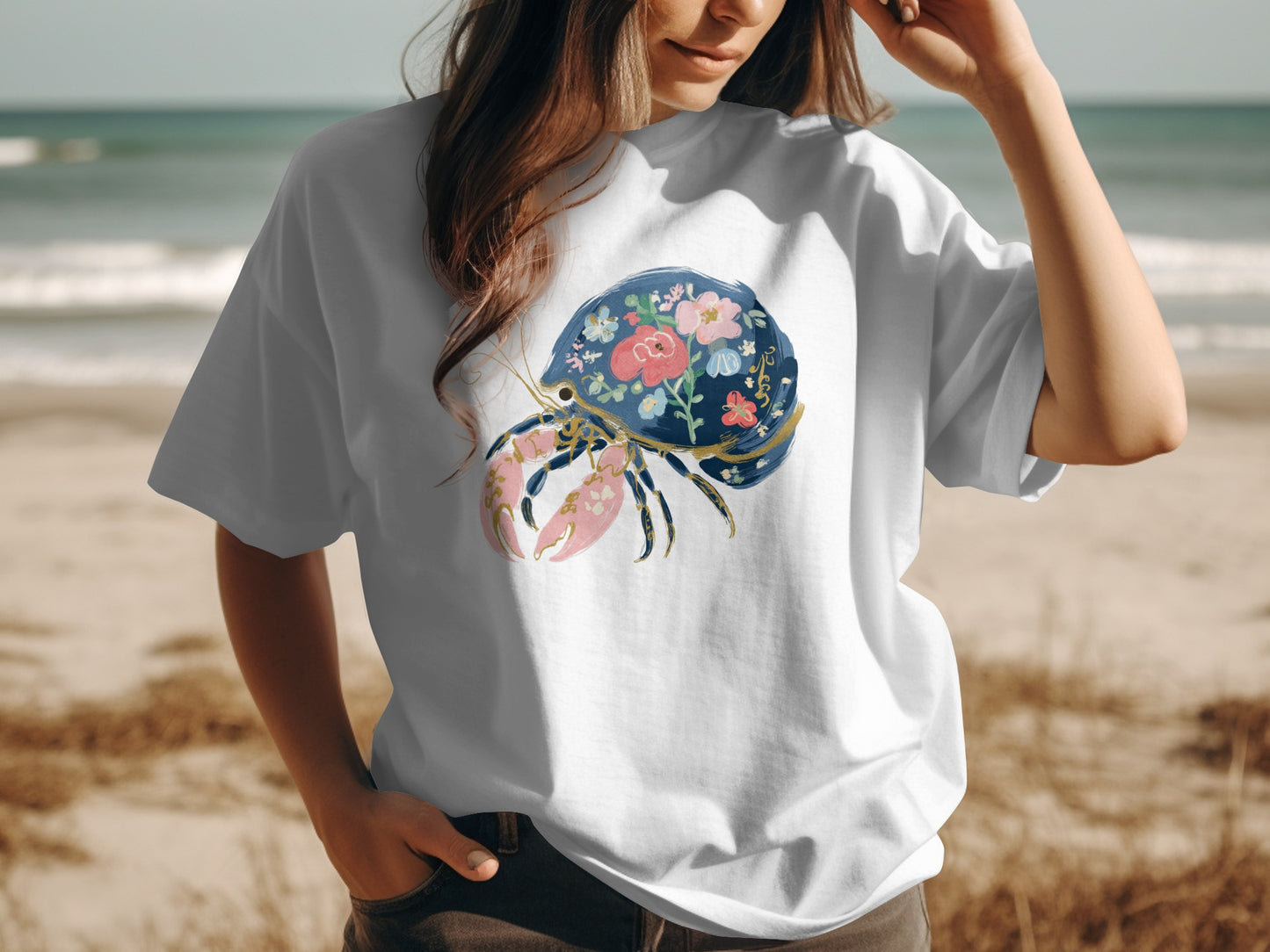 White t-shirt with a blue crab and floral design on a beach background.