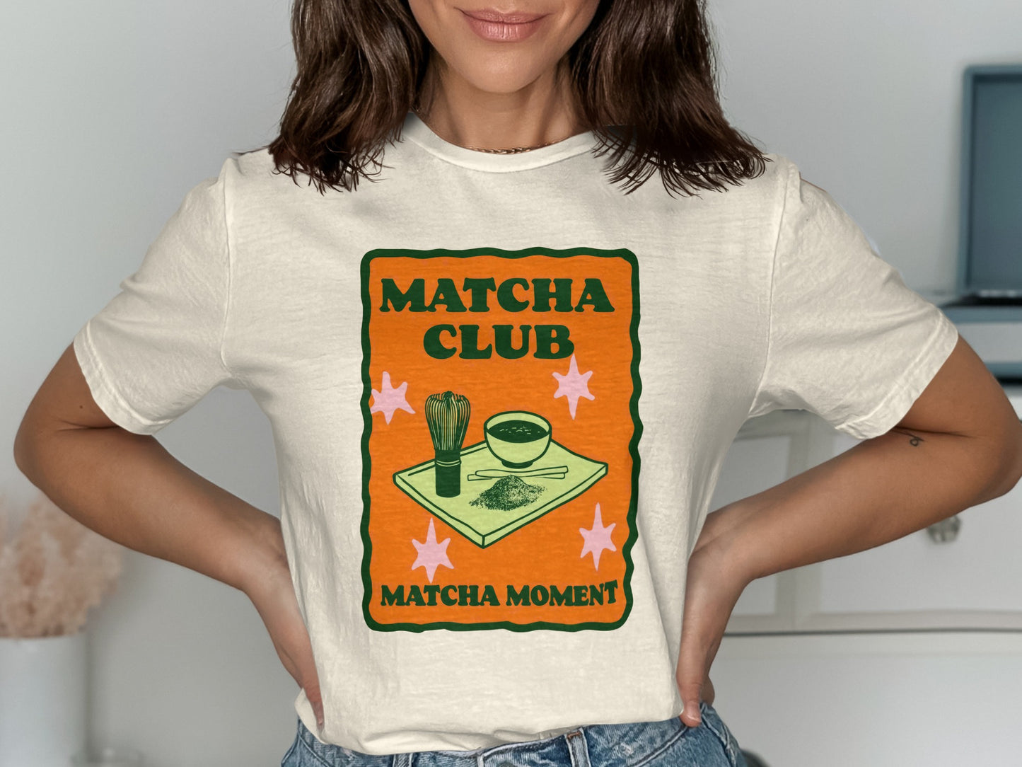 "Matcha Club Matcha Moment" text on a cream t-shirt with matcha bowl and whisk graphic.
