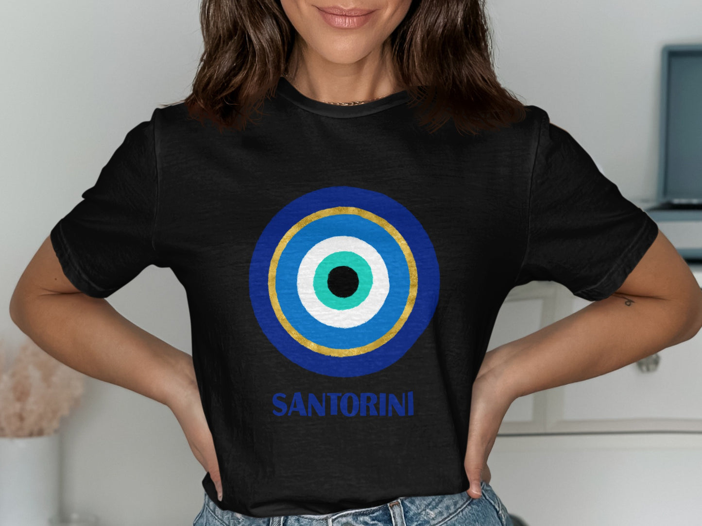 Black t-shirt with a blue, white, and gold evil eye design and "SANTORINI" text.