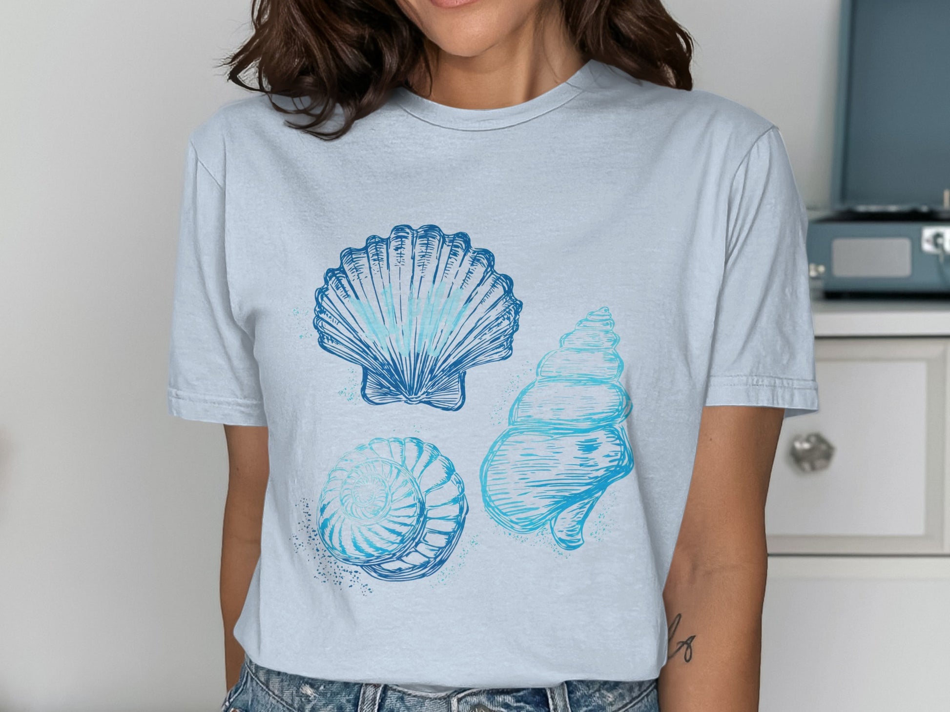 Light blue t-shirt with graphic of three blue watercolor seashells.