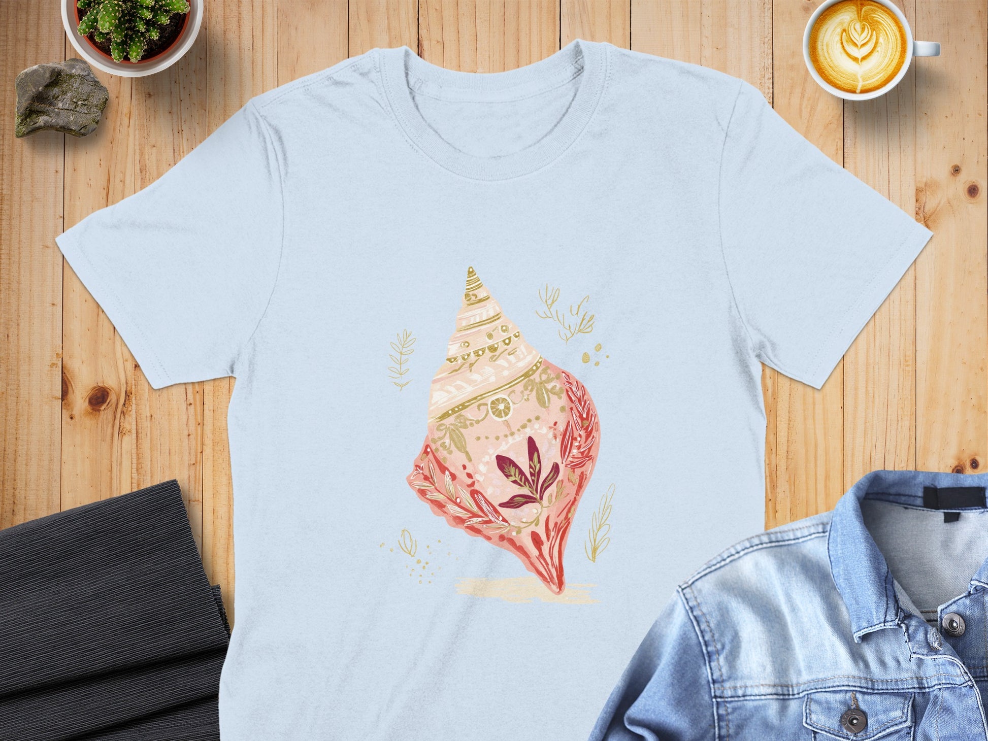 Light blue t-shirt with a pink and gold seashell graphic and floral accents.